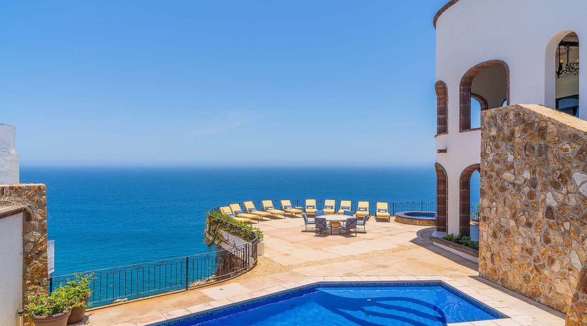 Stunning clifftop villa with private pool overlooking endless blue waters. Stone-clad architecture frames your sun-drenched terrace, where lounge chairs invite pure relaxation beneath the open sky.
