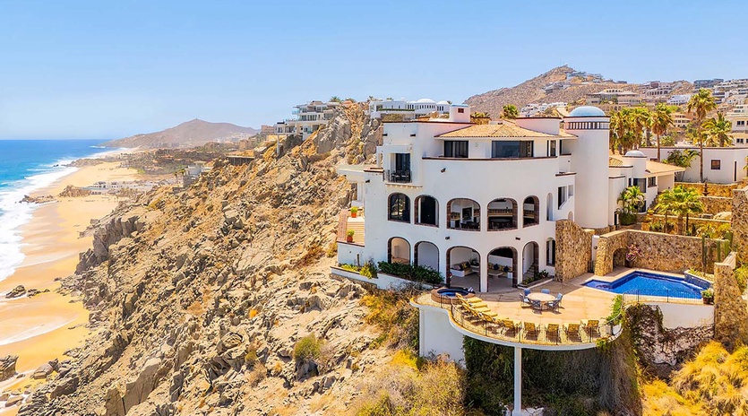 Stunning coastal villa perched on dramatic cliffs, featuring a private pool overlooking golden beaches and turquoise waters in a serene hillside setting.