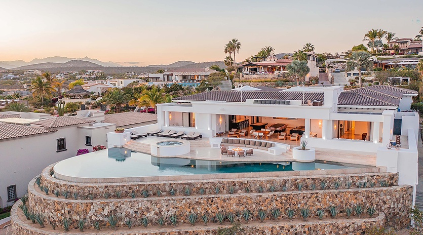 An elevated view of a stunning villa showcasing its contemporary design, terraced landscaping with natural stone walls, and luxurious outdoor living spaces set against mountains and tropical palms.