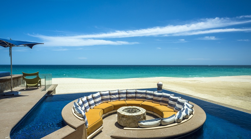 Stunning beachfront pool with sunken fire pit seating area overlooking pristine white sand and turquoise waters.