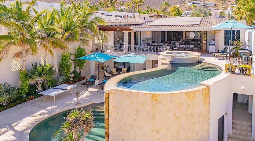 A luxurious desert retreat nestled in the hillside, featuring tiered pools, lush tropical gardens, and expansive terraces with dramatic mountain and residential views.
