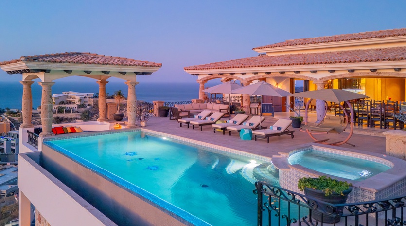 Stunning rooftop terrace with infinity pool, hot tub, and panoramic ocean views at dusk.