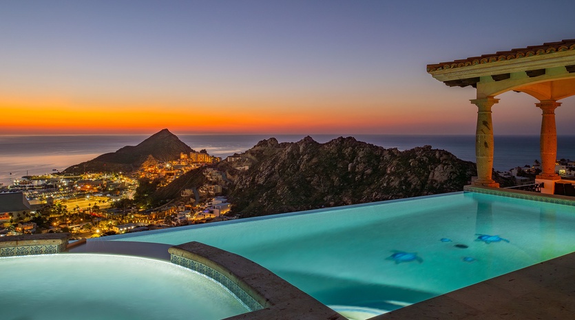 Stunning infinity pool overlooks coastal mountains and city lights during golden sunset. Perfect evening setting with hot tub.