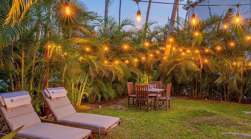Relax on cushioned lounge chairs in your private garden, where tropical palms and warm string lights create an enchanting retreat for evening dining or stargazing under the open sky.
