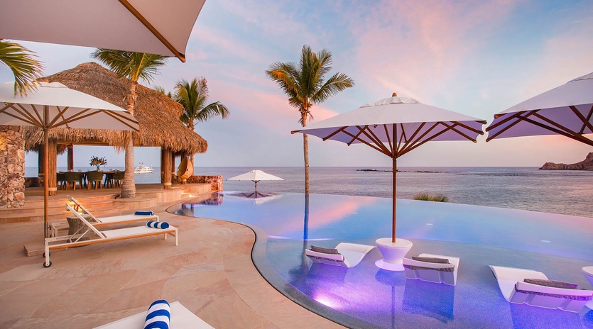 A stunning infinity pool merges with ocean views as sunset paints the sky in soft pastels, creating a serene paradise where relaxation meets tropical luxury.