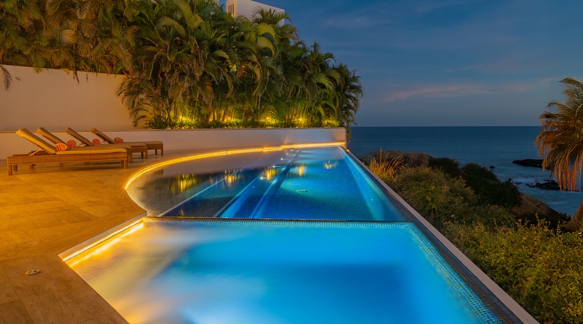 Luxurious oceanfront pool with dramatic evening lighting and panoramic sea views creates an unforgettable tropical escape.