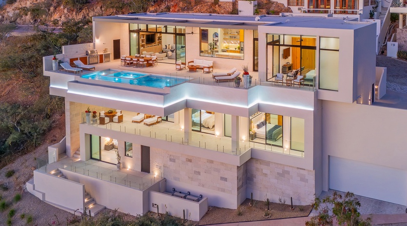 A stunning multi-level modern villa featuring illuminated terraces, infinity pool, and panoramic hillside positioning.