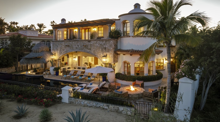 Elegant Mediterranean villa with stone archways, tropical gardens, poolside fire pit, and warm evening lighting creating the perfect luxury retreat.
