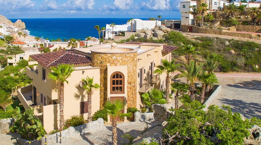 A stunning beachfront villa nestled among palm trees and natural landscaping, with sweeping ocean views and the sparkling Sea of Cortez beyond.