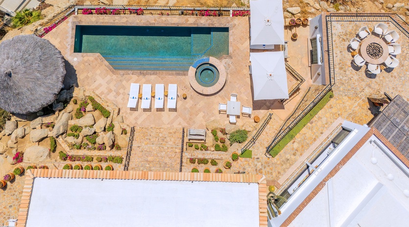Aerial view of the property showcasing a pristine swimming pool, hot tub, outdoor dining areas, and landscaped grounds with mountain terrain backdrop.