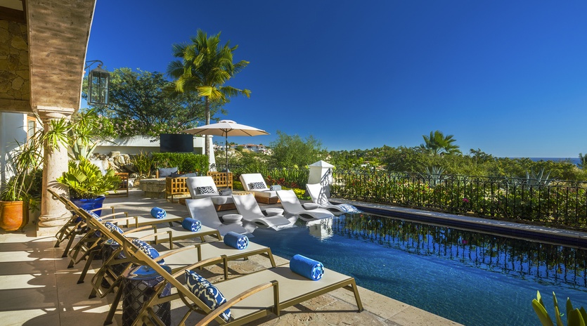 Luxurious infinity pool terrace with premium loungers overlooking lush tropical gardens under endless blue skies.