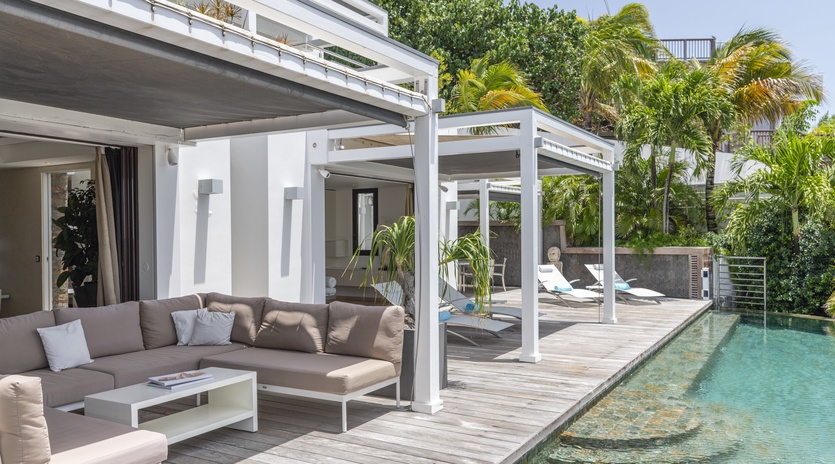 Your private poolside terrace invites you to lounge under a pergola surrounded by lush tropical palms and modern outdoor seating.
