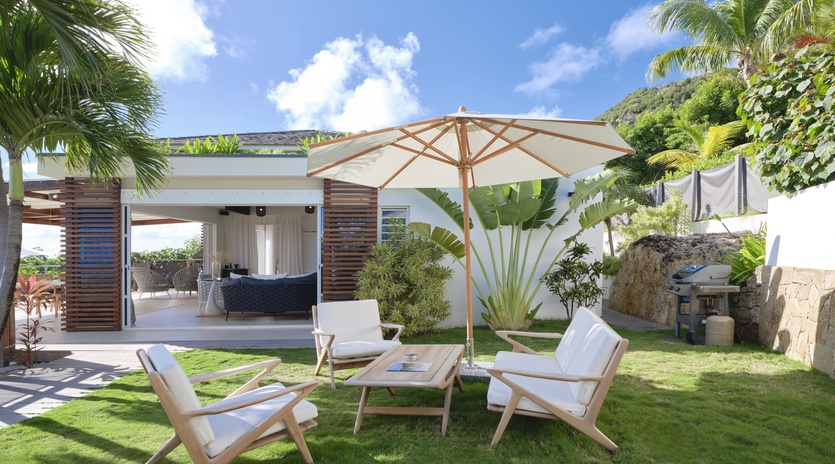 Unwind in your private tropical garden with comfortable lounge chairs under a stylish umbrella, surrounded by lush palms and vibrant greenery.