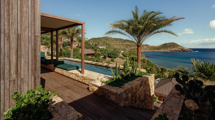 Modern villa featuring private pool, wooden decking, and tropical landscaping overlooking crystal blue waters and coastal hills.