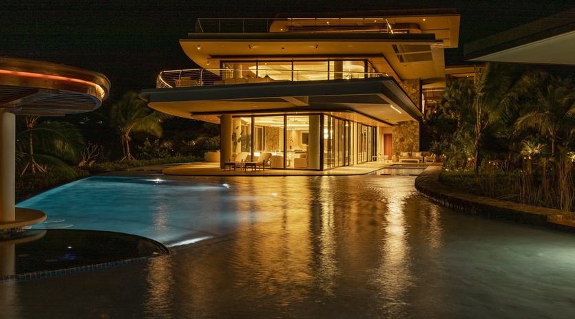 Modern luxury villa showcasing contemporary architecture with illuminated pool and tropical landscaping during evening hours.