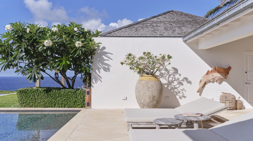 Sunlit poolside paradise with elegant loungers, tropical gardens, and tranquil ocean beyond—your private retreat awaits.