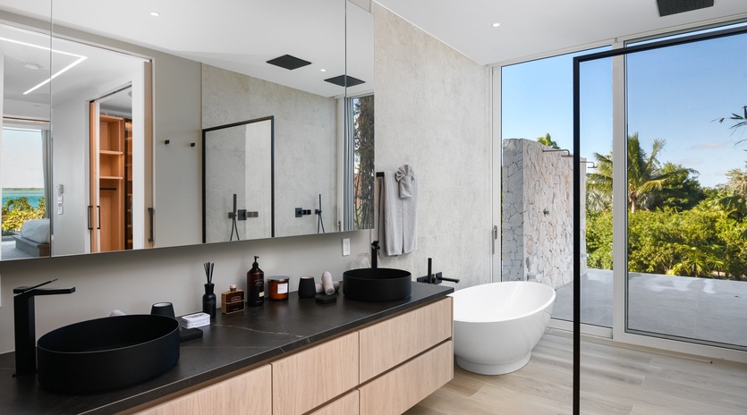 Step into your private spa-like sanctuary, where sleek black fixtures and a freestanding soaking tub await. Natural light floods in through floor-to-ceiling glass, framing lush tropical views while you unwind.