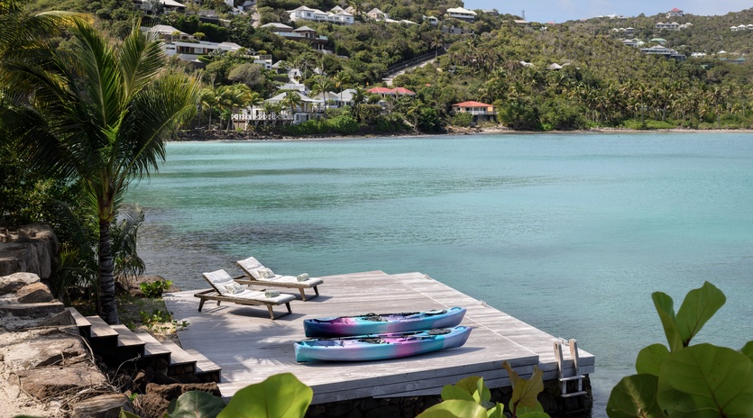 Private waterfront dock with kayaks and lounge chairs overlooking crystal-clear turquoise waters and tropical hillside community.