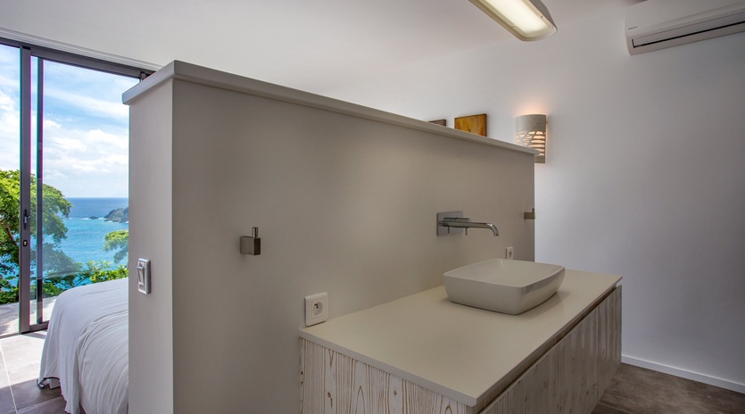 Modern bathroom with sea views through floor-to-ceiling windows, featuring a floating vanity and sleek vessel sink.