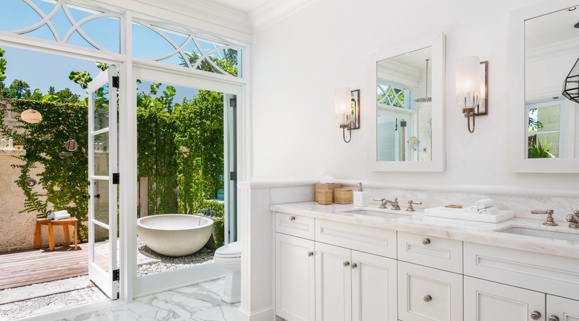 Elegant marble bathroom with double vanities opens to your private outdoor sanctuary, complete with a luxurious soaking tub surrounded by lush greenery and natural light.