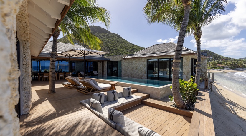 Luxurious beachfront villa featuring pristine white sand beach, swaying palm trees, and stunning mountain backdrop creating the perfect tropical paradise.
