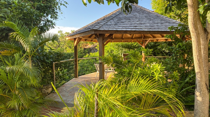 A tropical garden gazebo surrounded by lush palms and mature trees creates a peaceful outdoor retreat.