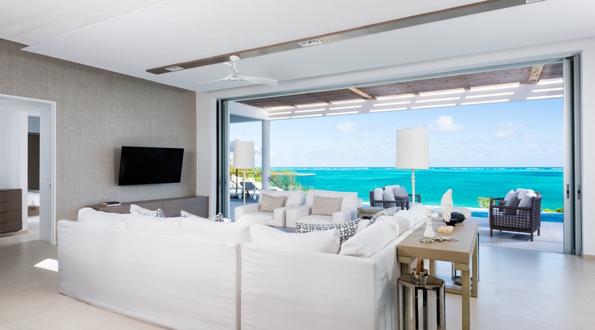 Sink into plush white sofas as ocean breezes drift through your open terrace doors, framing endless turquoise waters in your personal paradise.