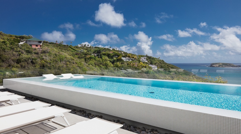Stunning infinity pool with crystal-clear waters and breathtaking sea views across lush tropical hillsides.