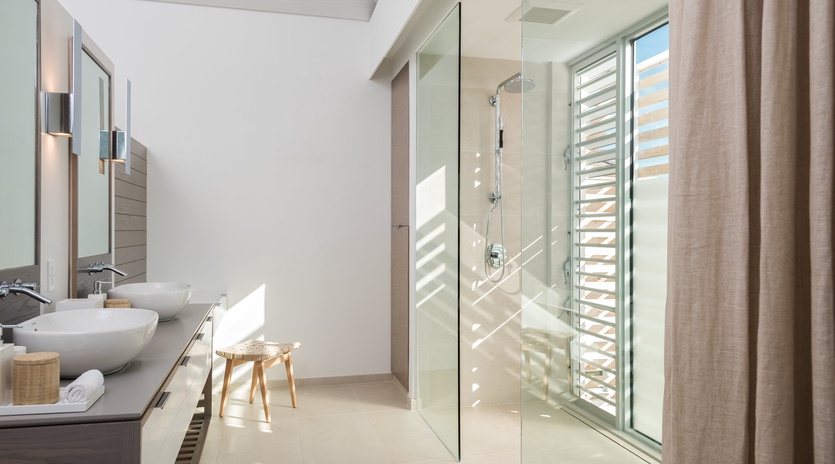 Step into your bright, modern bathroom sanctuary with a luxurious glass-enclosed shower and natural light streaming through elegant wooden blinds.