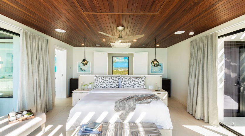 Sink into crisp linens under a stunning wood-paneled ceiling, where coastal artwork and soft natural light create your serene island retreat.
