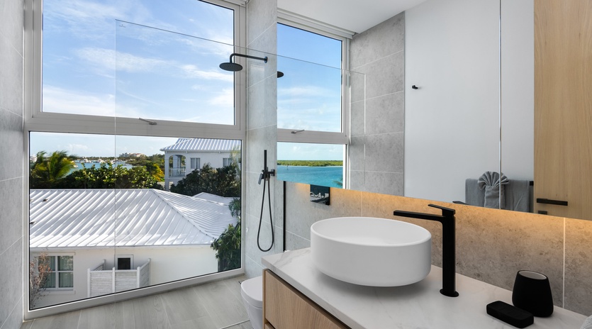 Your private bathroom frames tranquil water views through expansive windows, where modern fixtures meet coastal serenity. Crisp tiles and natural light create a spa-like escape for your morning routine.