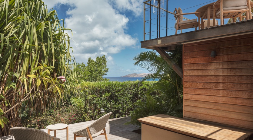 A modern wooden deck features tropical garden views and glimpses of distant coastal mountains, creating a peaceful outdoor retreat area.