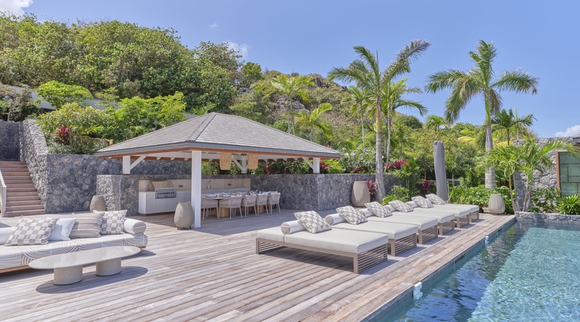 Luxurious poolside paradise with pristine swimming pool, elegant lounge beds, covered dining pavilion, and lush tropical landscaping.