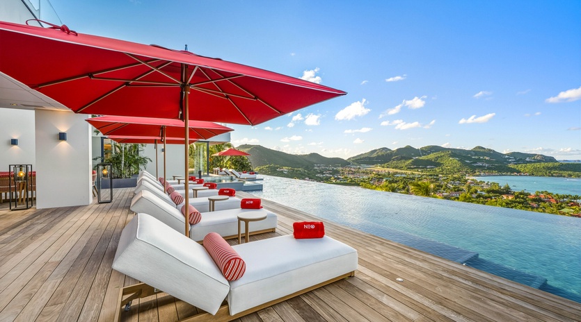 Relax on plush poolside loungers under vibrant red umbrellas while soaking in breathtaking mountain and sea views.