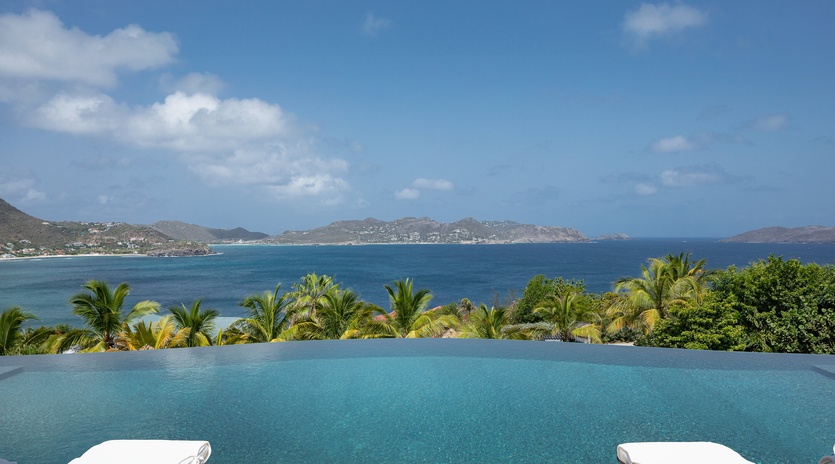 An infinity pool frames sweeping views of turquoise waters, lush palms, and distant coastal mountains under open Caribbean skies.