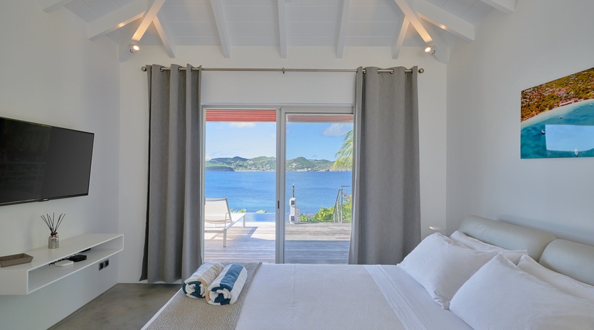 Wake up to stunning ocean views from your private bedroom, where modern comfort meets tropical elegance with exposed beams and terrace access.