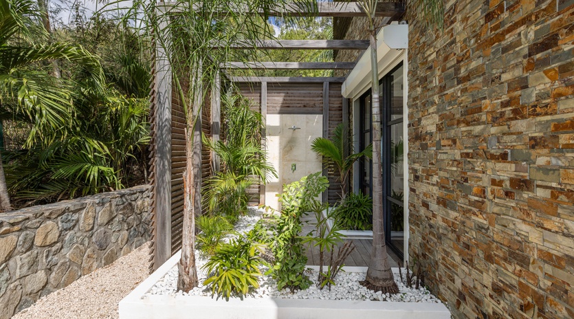 Modern tropical entrance with natural stone walls and lush landscaping creates a serene arrival experience.