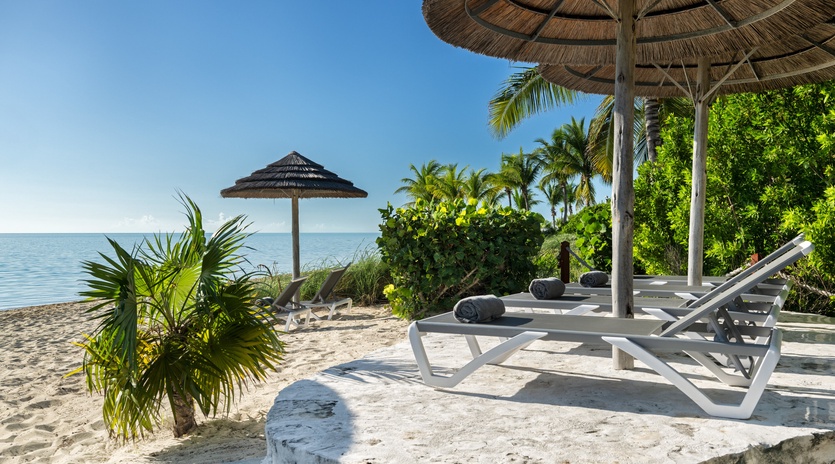 Your private beachfront paradise with loungers under thatched umbrellas, where soft sand meets crystal-clear waters for ultimate relaxation.