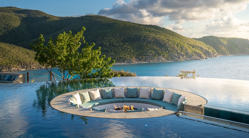 Spectacular infinity pool with sunken seating area overlooking pristine turquoise waters and lush mountains.