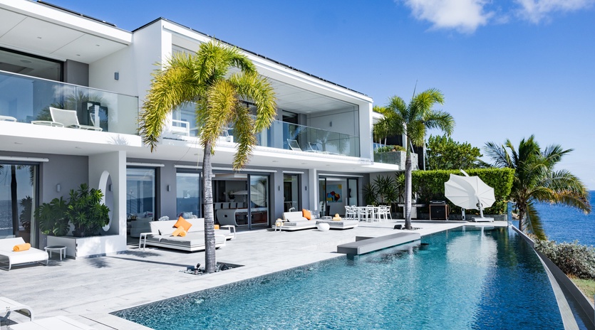 Sleek modern villa featuring pristine swimming pool, tropical landscaping, and contemporary architecture under clear blue skies.