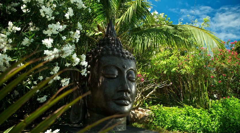 A serene Buddha statue sits nestled among tropical blooms and palm fronds, creating your own peaceful meditation sanctuary.