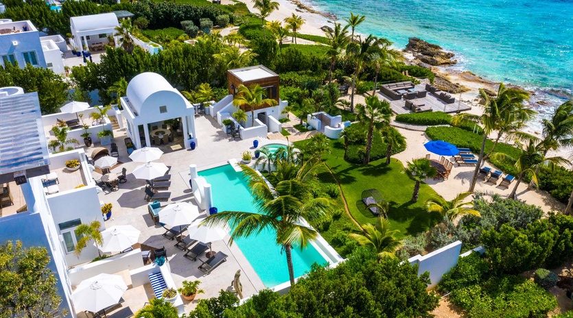 Beachfront villa complex with twin pools, lush tropical gardens, and pristine turquoise waters of the Caribbean coastline.