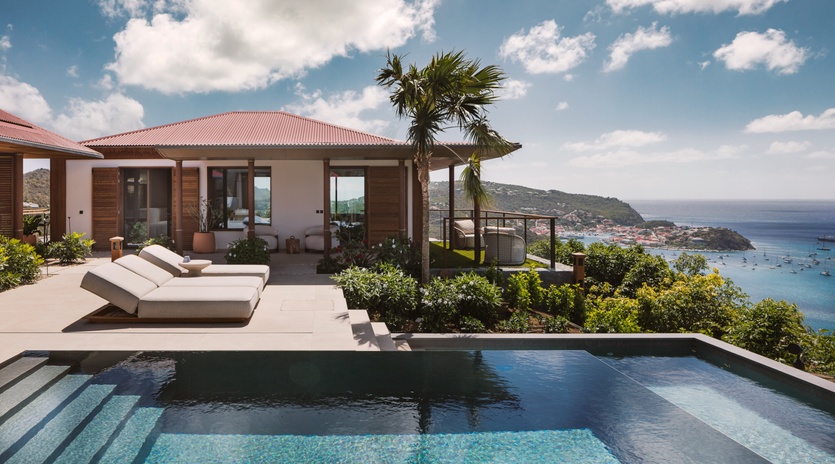 Modern villa overlooking turquoise Caribbean waters with infinity pool and tropical hillside setting.