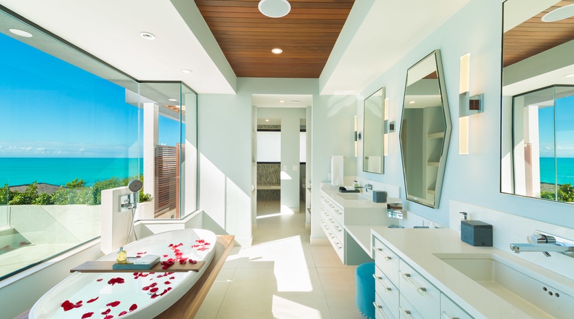 Soak in pure tranquility as sunlight streams through floor-to-ceiling windows, revealing breathtaking turquoise waters. Rose petals drift in your tub while warm wood tones and spa-like serenity surround you.