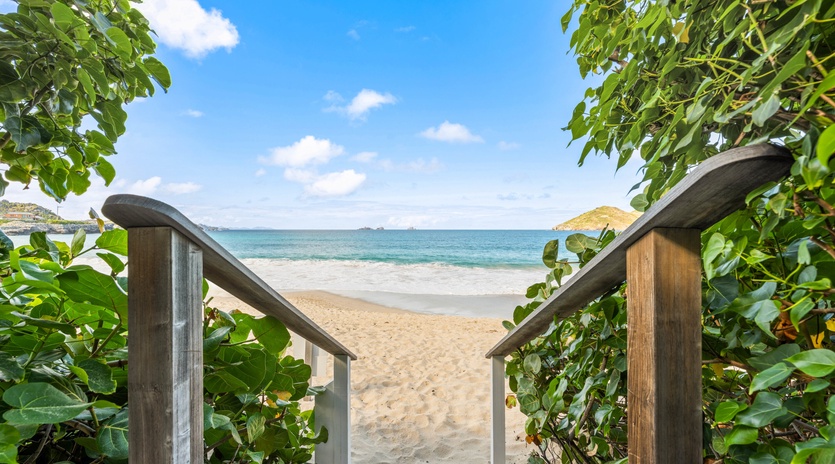 Private wooden boardwalk leads through lush tropical foliage to pristine sandy beach and crystal-clear waters.