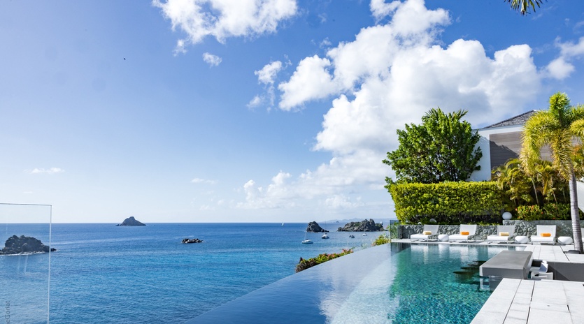 Stunning infinity pool overlooking pristine Caribbean waters with tropical landscaping and modern outdoor seating areas.