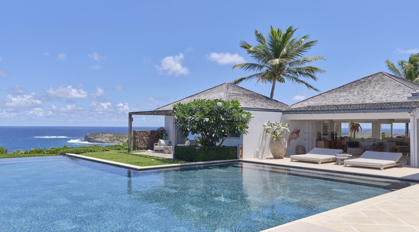 A stunning oceanfront villa with an infinity pool stretching toward endless blue waters. Swaying palms and open-air lounging areas frame your private tropical paradise.