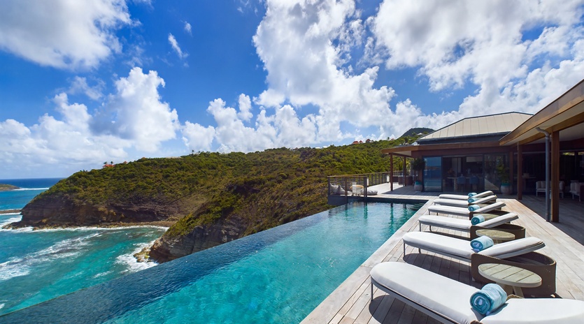 Infinity pool overlooking dramatic coastline with pristine turquoise waters and lush hillsides on a perfect sunny day.