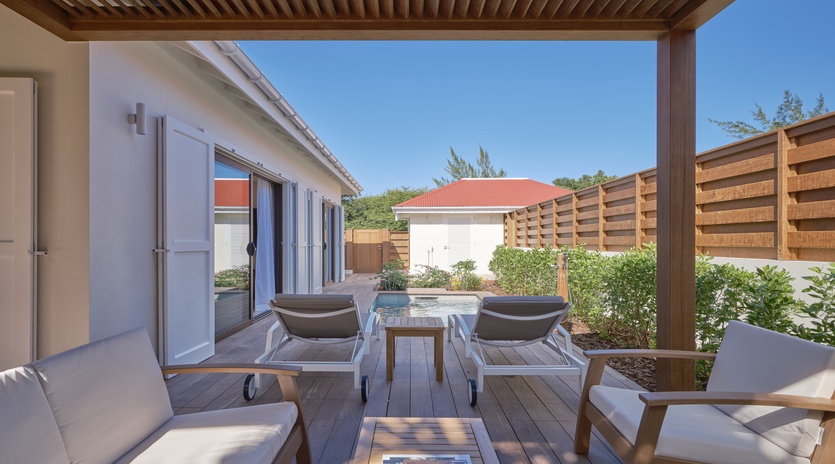 Unwind on your private terrace with modern seating, soothing hot tub, and beautiful garden views under peaceful blue skies.