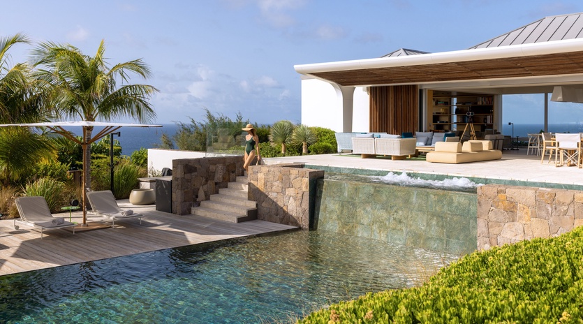 Modern luxury villa with infinity pool cascades into ocean views, surrounded by tropical palms and contemporary architecture.